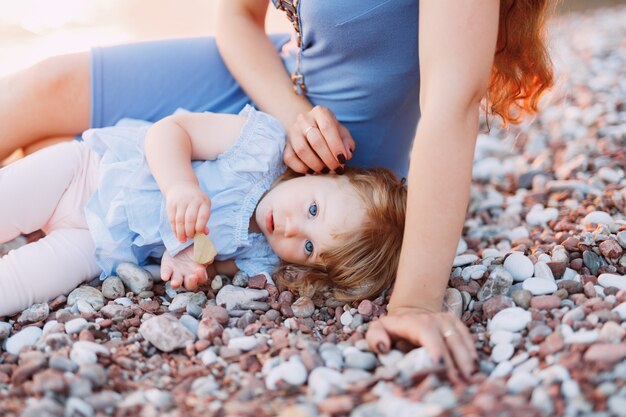 Petite fille se trouve près de sa mère sur une plage de galets.