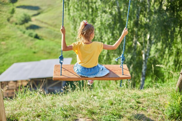 Petite fille semblant se balançant sur une grande balançoire en bois rustique dans le parc, lumière du soleil