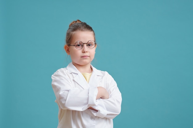 Petite fille sérieuse aux bras croisés en blouse blanche et lunettes