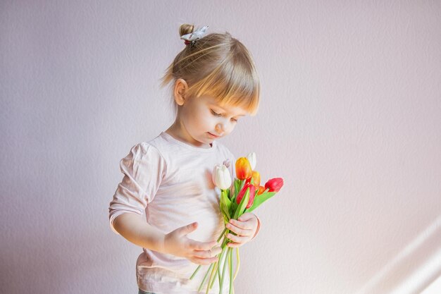 Une petite fille sérieuse tient un bouquet de tulipes colorées dans les mains