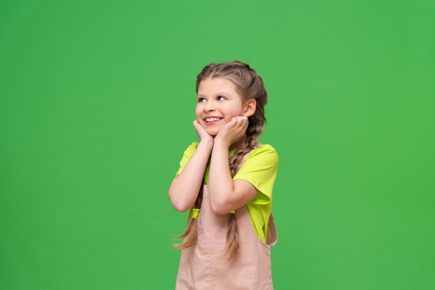 La petite fille serre ses joues et sourit à un enfant avec des nattes sur un fond vert isolé