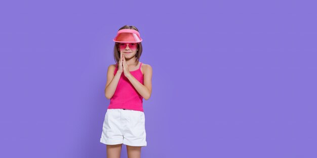 Une petite fille en short blanc, un tee-shirt rose, des lunettes tendance roses et une visière d'été