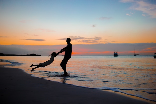 Petite fille et silhouette du père heureux au coucher du soleil à la plage