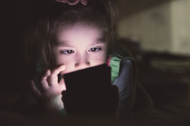 Petite fille avec smartphone allongée dans un lit,