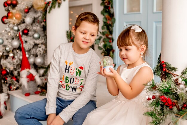 Petite fille et son frère ouvrent des cadeaux de Noël. Les enfants voient une boule à neige surprise