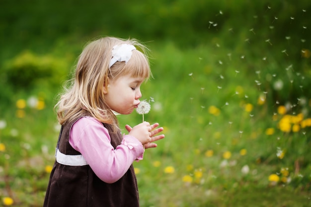 La petite fille souffle un pissenlit