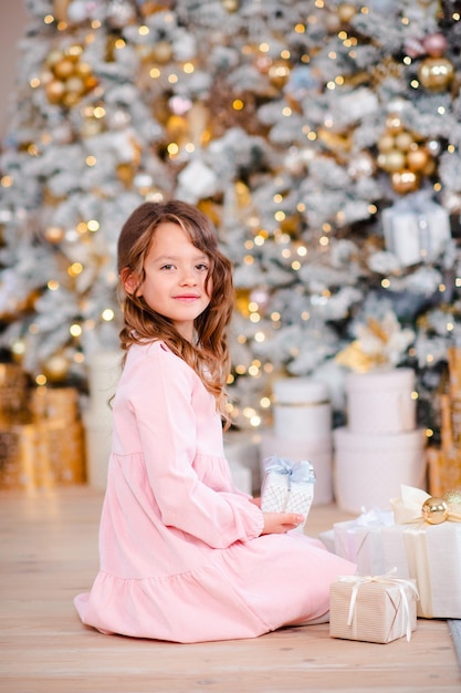 Petite fille souriante de 5 à 6 ans présente sous l'arbre de Noël sur fond de lumières t dans la chambre