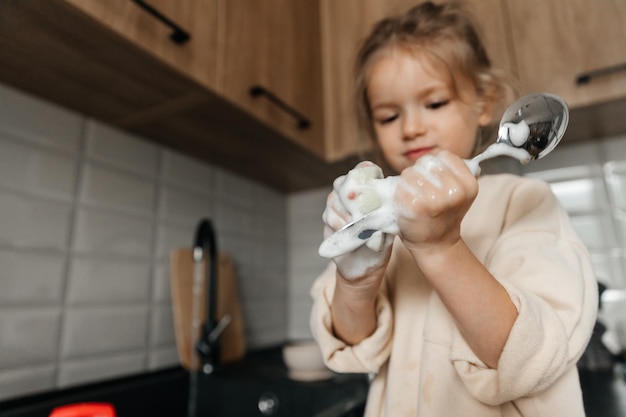 Une petite fille souriante aide aux tâches ménagères et lave la vaisselle dans la cuisine