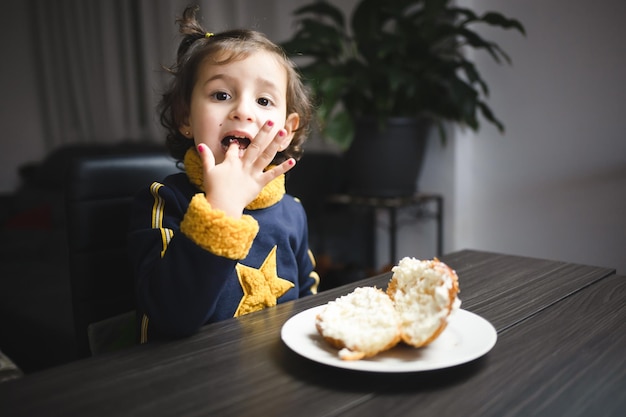 Petite fille souriante alors qu'elle se salit en mangeant un chou à la crème