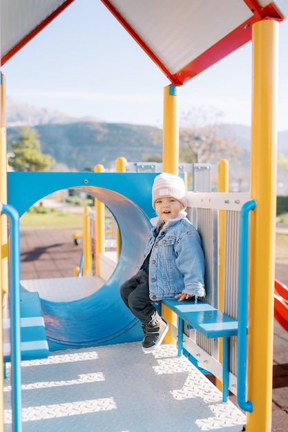 Une petite fille souriante assise sur un banc sur une glissière.