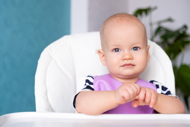 Petite fille souriante en bavoir rose sur chaise haute à la maison