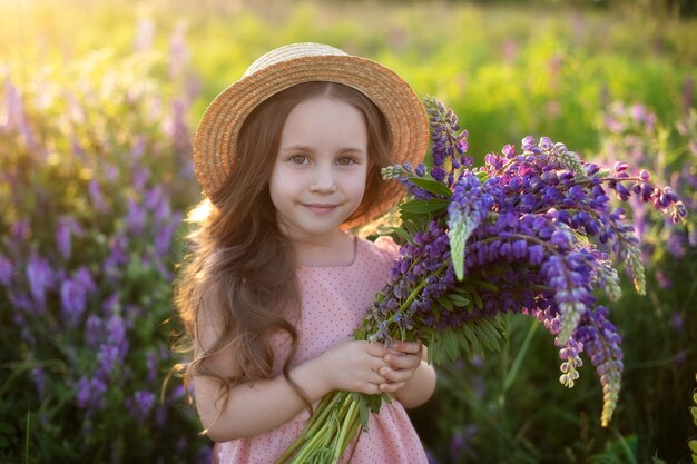 Petite fille souriante avec bouquet de lupins dans une prairie d'été une fillette dans un champ de lupins