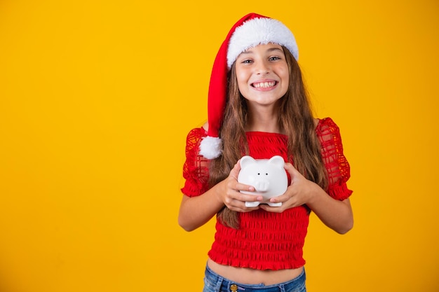 Petite fille souriante avec un chapeau de noël tenant une tirelire