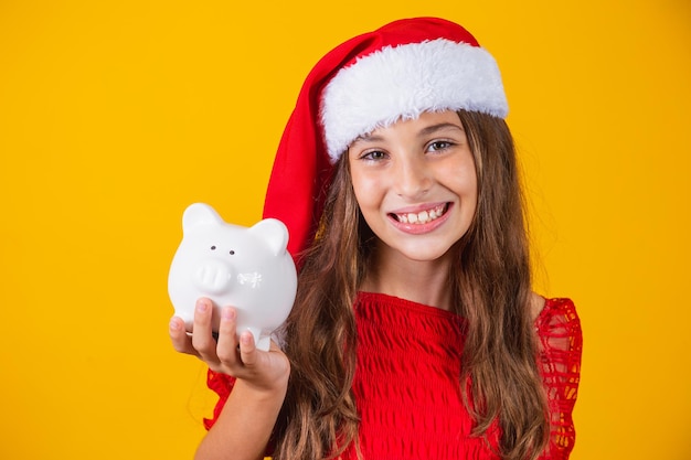 Petite fille souriante avec un chapeau de noël tenant une tirelire