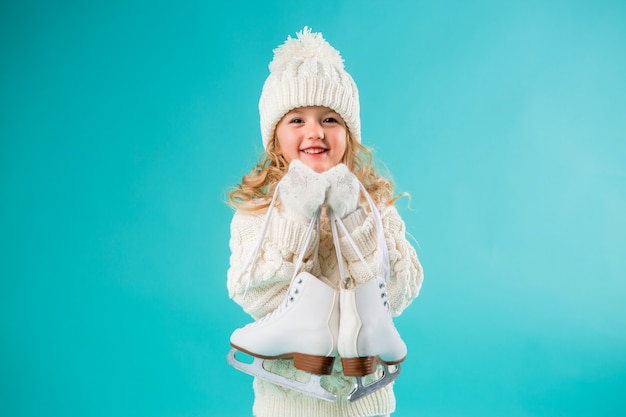 petite fille souriante dans un chapeau blanc d'hiver et un pull, tenant des patins