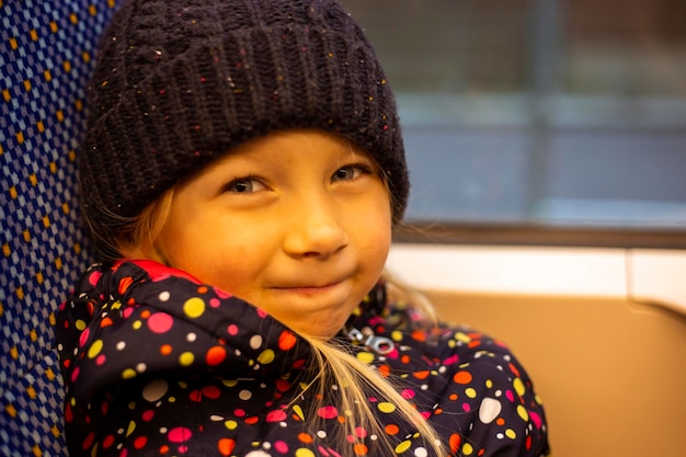 Une petite fille souriante dans un chapeau est assise dans un transport urbain