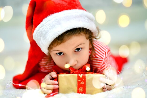 Une petite fille souriante dans le chapeau rouge du Père Noël et des vêtements de Noël rouges avec un cadeau Nouvel An Noël