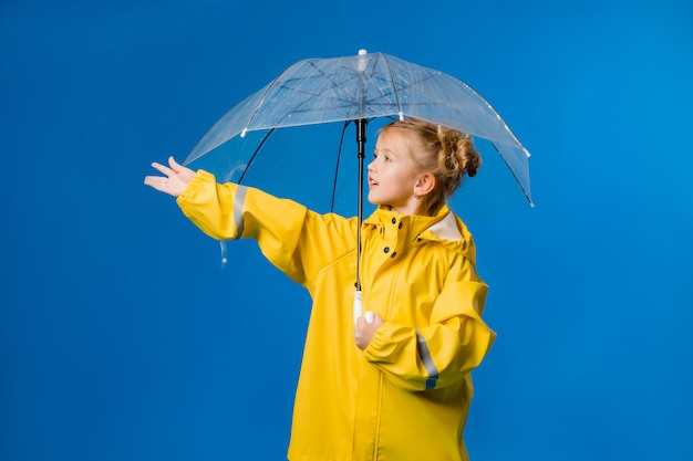 Petite fille souriante dans un imperméable jaune et des bottes en caoutchouc avec un parapluie