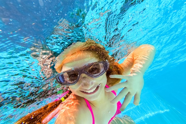 Petite fille souriante dans des lunettes de natation nageant sous l'eau dans la piscine