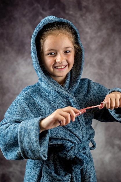 Petite fille souriante dans une robe de chambre et une brosse isolée sur fond gris