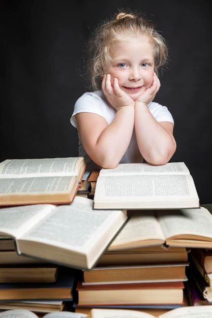 Petite fille souriante est assise avec une pile de livres Éducation et formation des enfants Fond noir Vertical