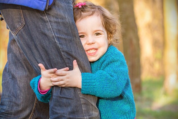 Petite fille souriante et étreignant la jambe de papa, famille