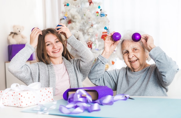 Petite-fille souriante et grand-mère jouant avec des boules décoratives à Noël