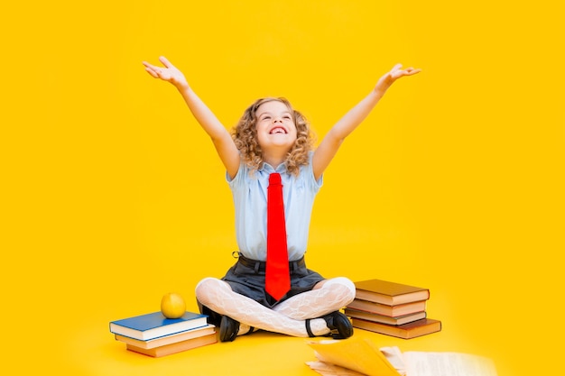 Une petite fille souriante et heureuse en uniforme scolaire est assise avec des livres,