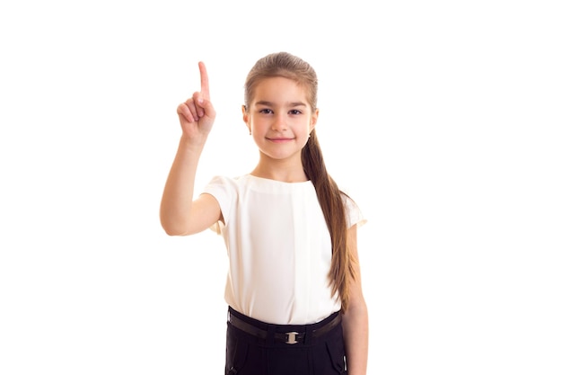 Petite fille souriante avec une longue queue de cheval brune en T-shirt et jupe sur fond blanc en studio