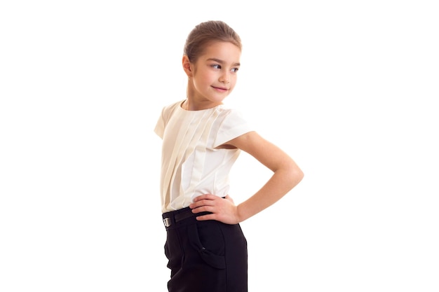 Petite fille souriante avec une longue queue de cheval brune en T-shirt et jupe sur fond blanc en studio