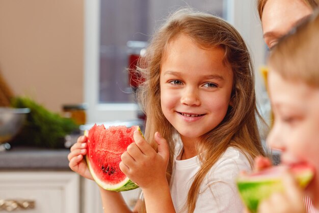 Petite fille souriante mangeant une tranche de pastèque dans la cuisine