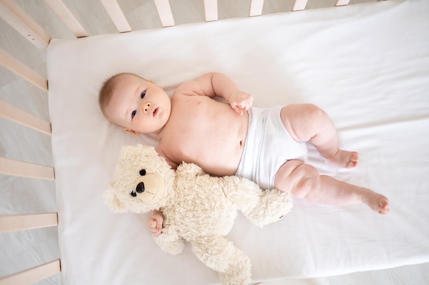 Une petite fille souriante mignonne en culotte blanche est allongée dans un berceau à la maison sur le dos en regardant la caméra en souriant bébé heureux