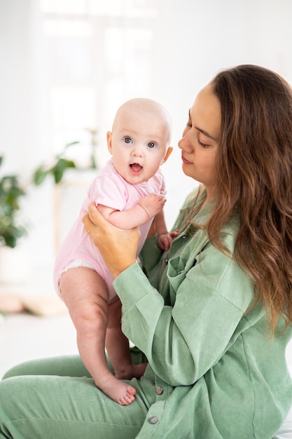 Une petite fille souriante mignonne dans un body rose dans les bras de sa mère dans la chambre à la maison câlins de maman et fille soins de bébé soins de maman