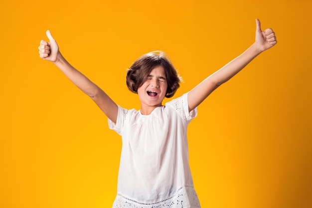 Une petite fille souriante montrant les pouces vers le haut geste sur un fond jaune concept de succès