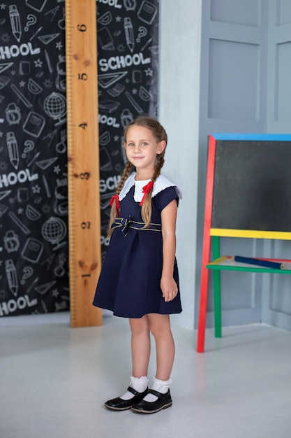 Une petite fille souriante avec des nattes et en uniforme scolaire se tient en classe à l'école