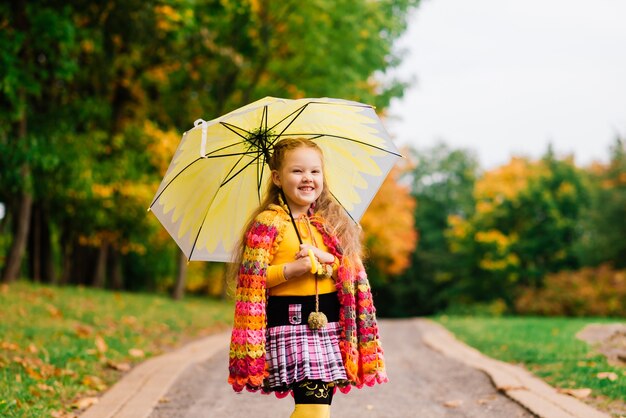 Petite fille souriante avec parapluie dans un imperméable et des bottes en plein air