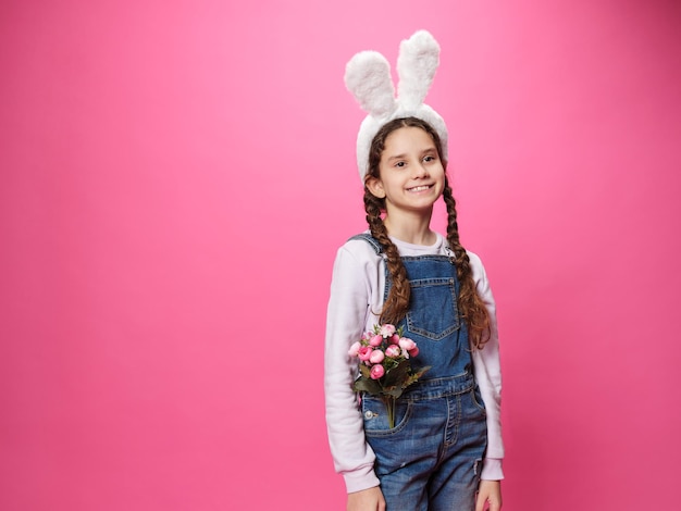 Petite fille souriante portant de jolies oreilles de lapin de Pâques souriant avec un visage heureux, elle a un bouquet de fleurs dans sa poche Espace pour le texte