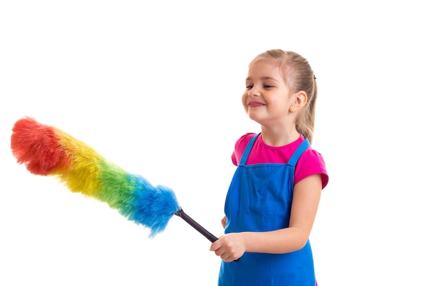 Petite fille souriante avec queue de cheval portant une chemise rose et un tablier bleu avec un plumeau coloré en studio