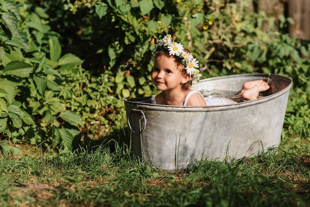 Une petite fille souriante se baigne dans une salle de bain pour enfants debout dans le jardin par une chaude journée d'été ensoleillée