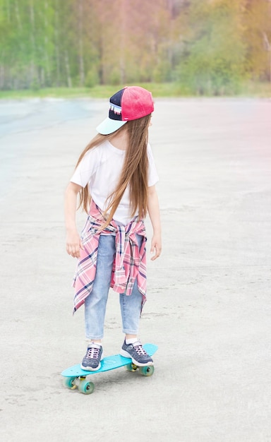 petite fille souriante se tient à l'extérieur avec une planche à roulettes dans ses mains sur le fond de la forêt