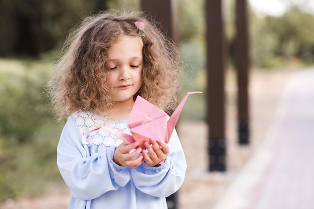 Petite fille souriante tenant un oiseau en papier origami dans le parc