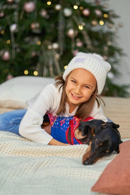 Petite fille souriante tout en tenant son chien à côté de l'arbre de Noël