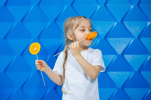 Petite fille avec un sourire et des nattes, vêtue d'un T-shirt blanc, tient une demi-orange à portée de main, concept d'un mode de vie sain