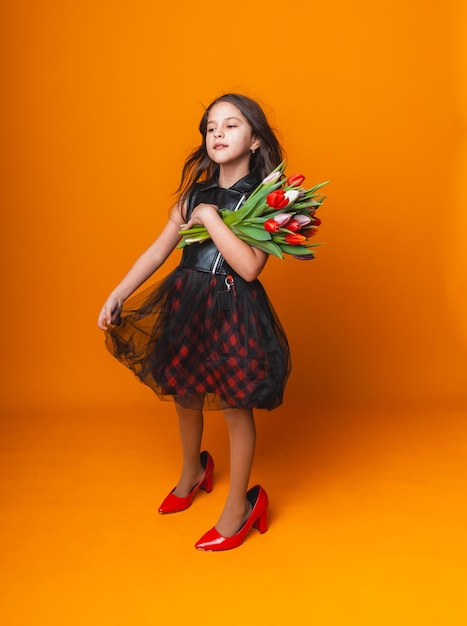 Petite fille sourit dans une robe et de grandes chaussures rouges tient un bouquet de fleurs sur un espace de fond jaune pour le texte