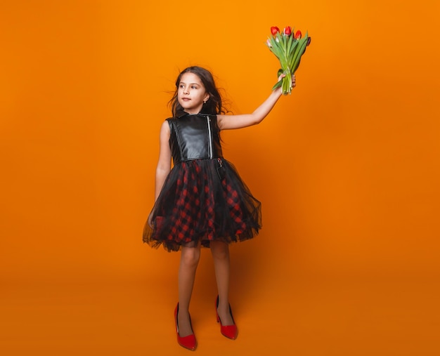 Petite fille sourit dans une robe et de grandes chaussures rouges tient un bouquet de fleurs sur un espace de fond jaune pour le texte