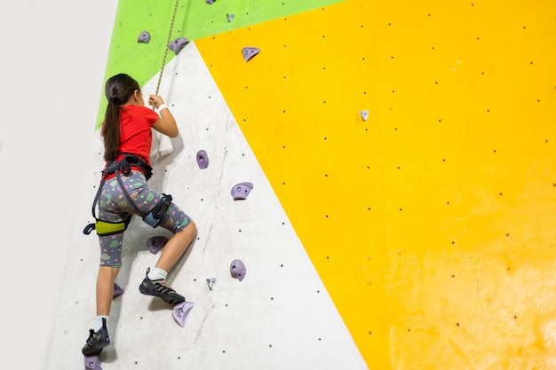 Petite fille sportive escalade rocher artificiel sur un mur pratique dans la salle de sport