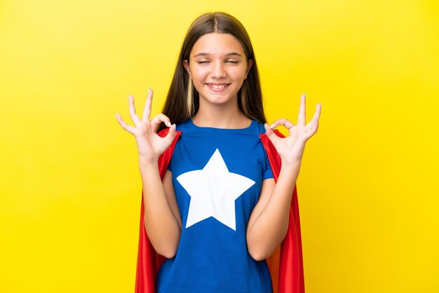 Petite fille de super-héros caucasien isolée sur fond jaune dans une pose zen