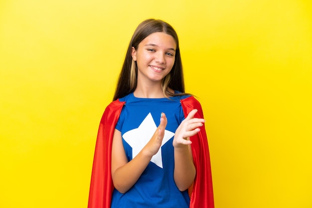 Petite fille de super-héros caucasienne isolée sur fond jaune applaudissant après présentation lors d'une conférence