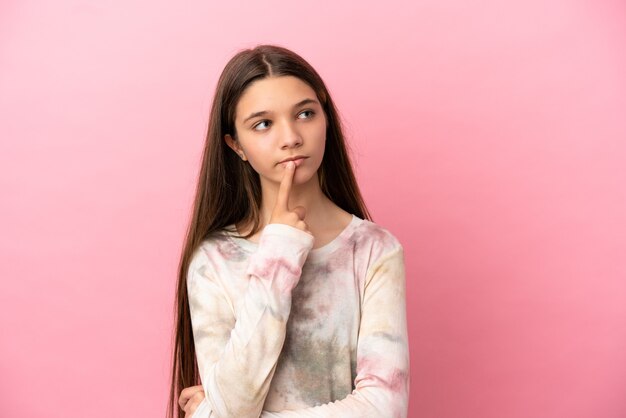 Petite fille sur une surface rose isolée ayant des doutes en levant les yeux