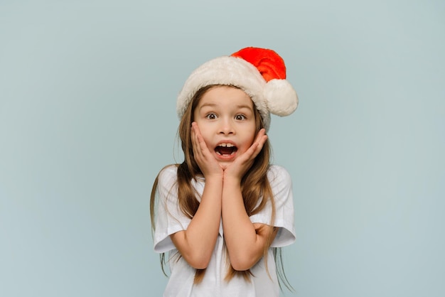 Petite fille surprise en bonnet de noel dit wow et regarde les ventes de Noël de l'appareil photo